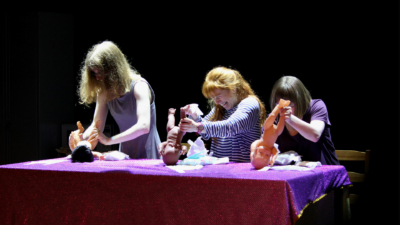 Three performers changing the nappies of three toy baby dolls
