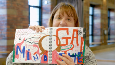 A person holding up an open notebook full of colourful drawings and words