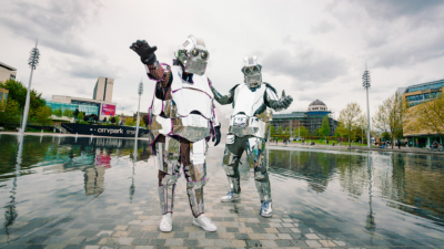 Two people wearing suits made of sheets of silver, resembling robots