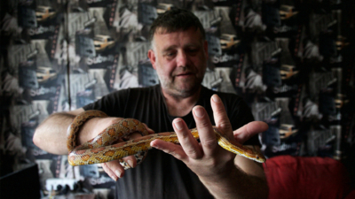 A person with short hair and a black t-shirt holding a small snake