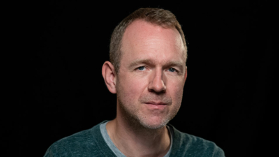 A headshot of Ben Pugh. He is a white middle aged man with short blonde hair and blue eyes. He is pictured against a dark background.