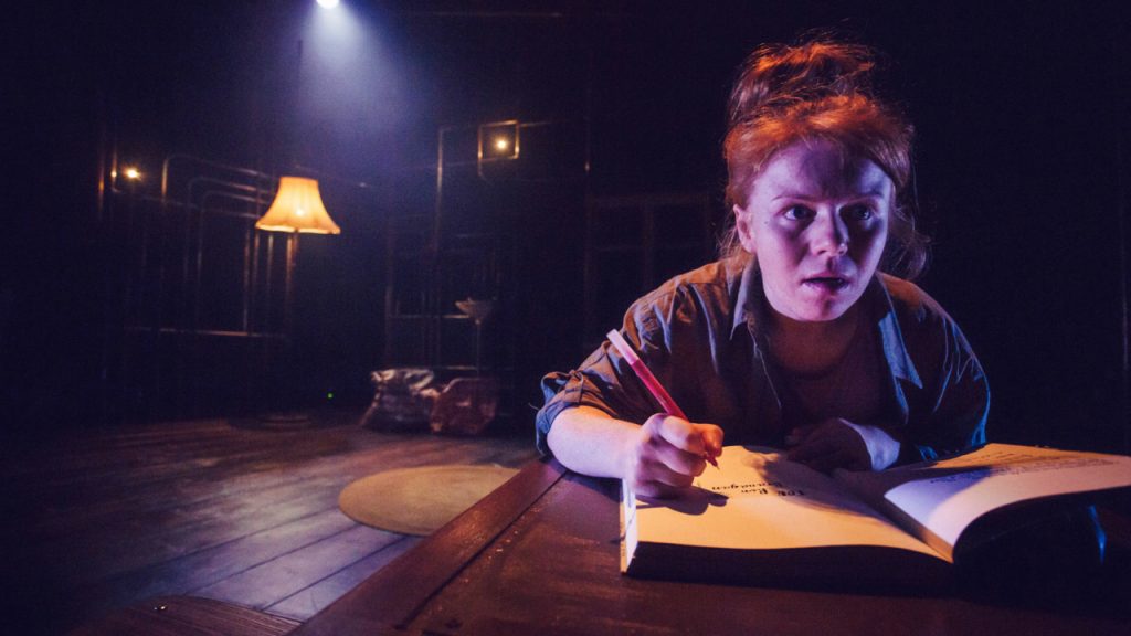 JoAnne Haines performing in A Little Space writing on a notebook